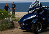 a blue spyder motorcycle in the foreground with a bikers couple walking holding hands on a beach in the background